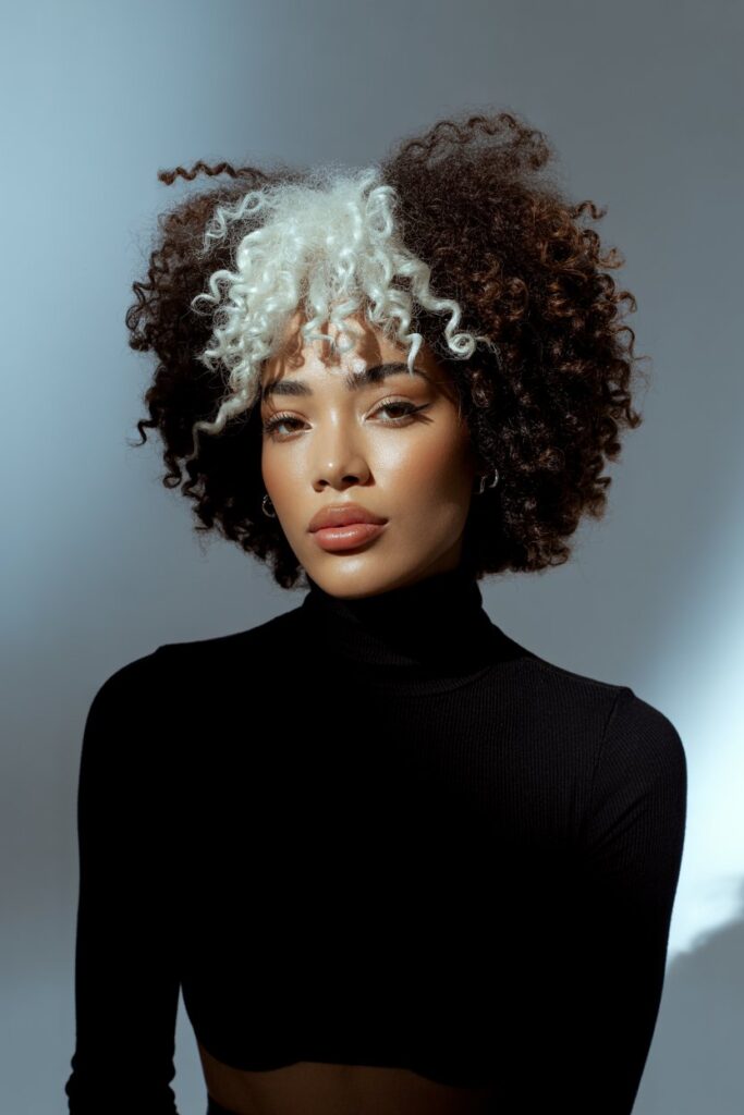 A stylish woman with coily natural afro-textured hair and crisp white front skunk stripe highlights,